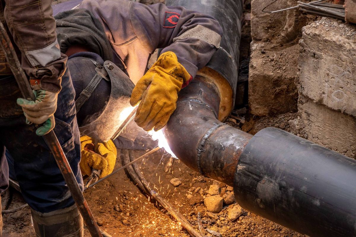A welder joining steel pipe on a construction site