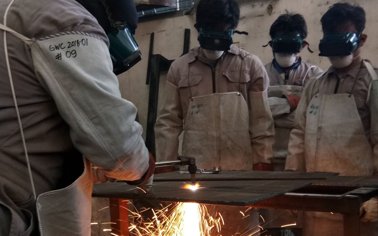 Technicians in protective gear watching a metal cut in a workshop in the Philippines